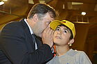Ein Mann flüstert einem Jungen mit gelber Kappe etwas ins Ohr