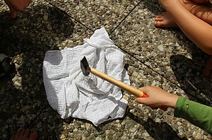 Kinderhände hauen mit einem Hammer auf ein Tuch