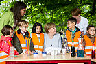 Angela Merkel gemeinsam mit Kindern in oranger Warnweste am Tisch