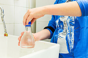 Eine Wasserflasche wird im Waschbecken aufgefüllt