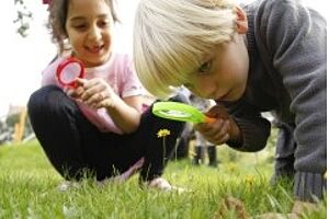 Zwei Kinder untersuchen eine Blumenwiese mit der Lupe