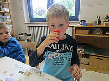 Ein Junge trinkt aus einem schmalen roten Gefäß