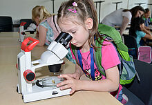 Einn Mädchen schaut durch ein Mikroskop
