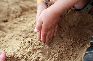 Zwei Kinderhände graben im Sand