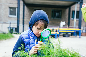 Ein Junge untersucht durch eine Lupe Pflanzen