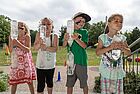 Vier Kinder mit Gesichtsbemalung halten zwei übereinandergestülpte Wasserflaschen in der Hand