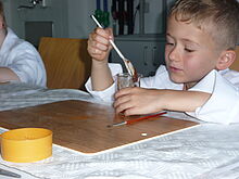 Ein Junge in weißem Kittel mischt Farbe mit einem Löffel zum Tag der kleinen Forscher in Chemnitz