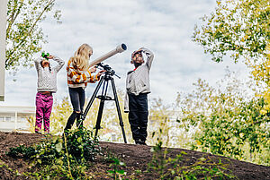 Drei Kinder stehen draußen mit einem Teleskop