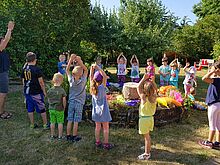 Kinder stehen in einem Kreis um ein buntes Beet udn heben ihre Arme
