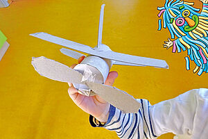 Eine Kidnerhand hält ein Papierflugzeug