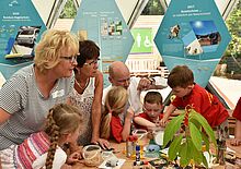 Drei Erwachsene untersuchen gemeinsam mit vier Kindern unterschiedliche Pflanzensamen.