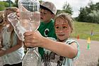 Ein Mädchen mit Schmetterlingsschminke im Gesicht installiert zwei Wasserflaschen übereinander