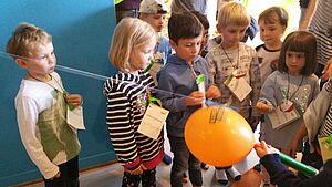 Kinder experimentieren zum Tag der kleinen Forscher mit einer Schnur, einem Luftballon und einer Röhre