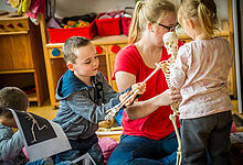 Zwei Kinder untersuchen gemeinsam mit einer Erzieherin ein Modell eines Skelletts